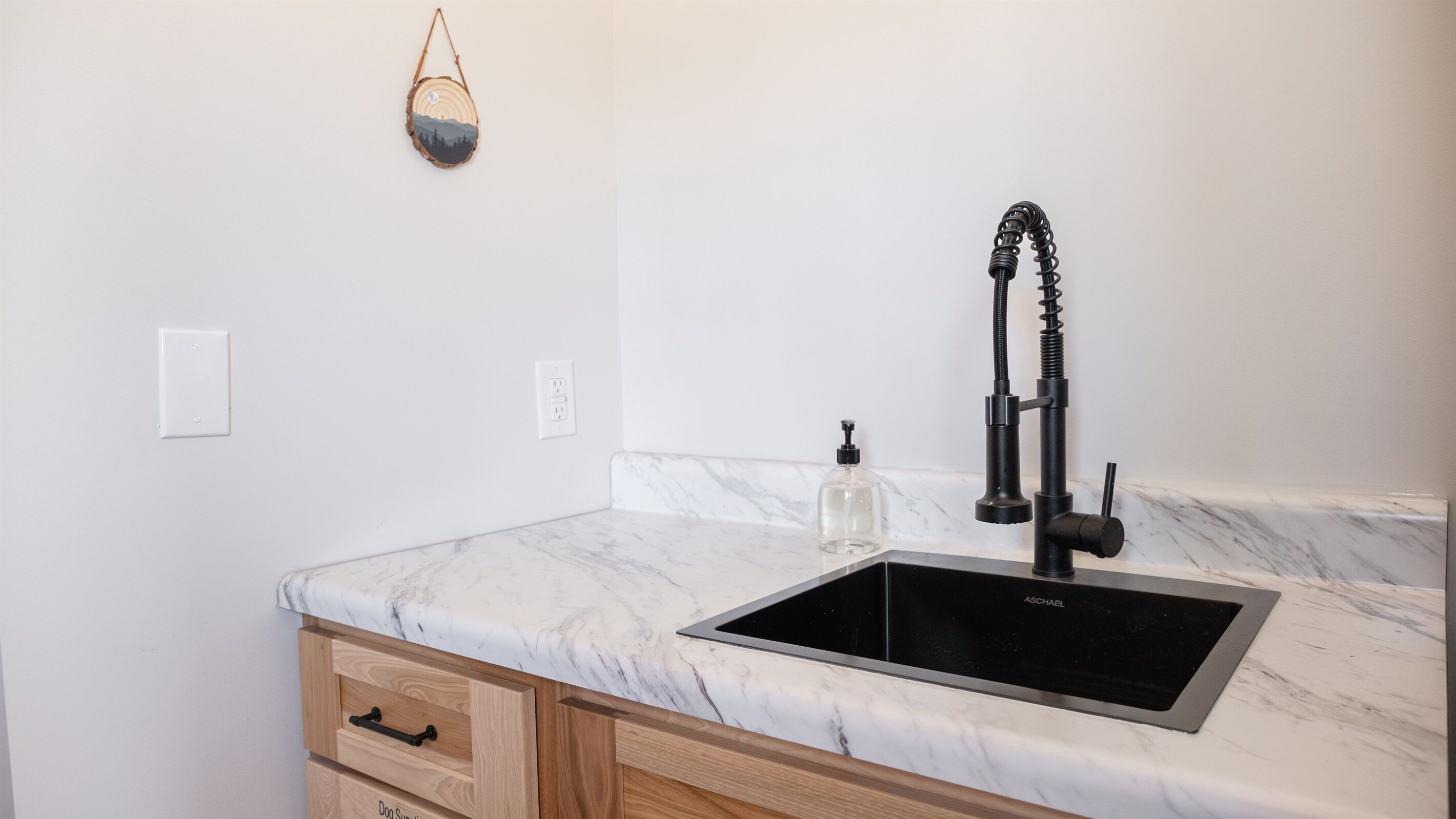A kitchen with a marble countertop, a black sink, wooden cabinets, and a hanging light fixture.