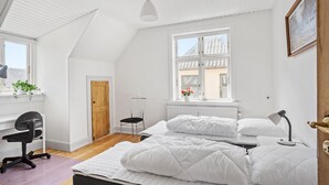 A bedroom with a large bed, a desk, a chair, and a window with a view of buildings.