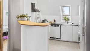 A modern kitchen with white cabinetry, a wooden countertop, a built-in dishwasher, and a window above the sink.