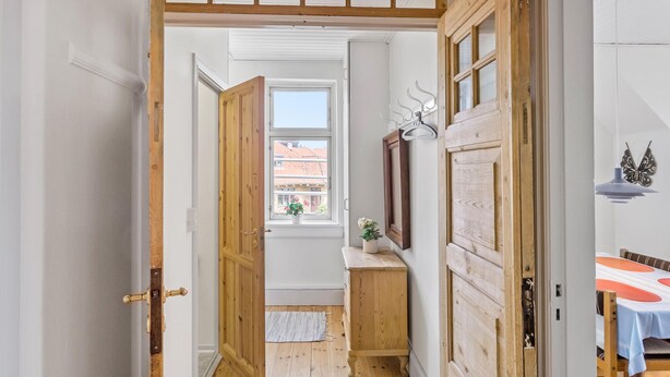 A narrow hallway with wooden doors and a window with a view of buildings.