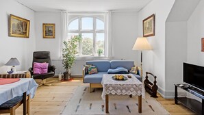 A living room with a blue sofa, a small table with a lace tablecloth, a television, and a window with curtains.