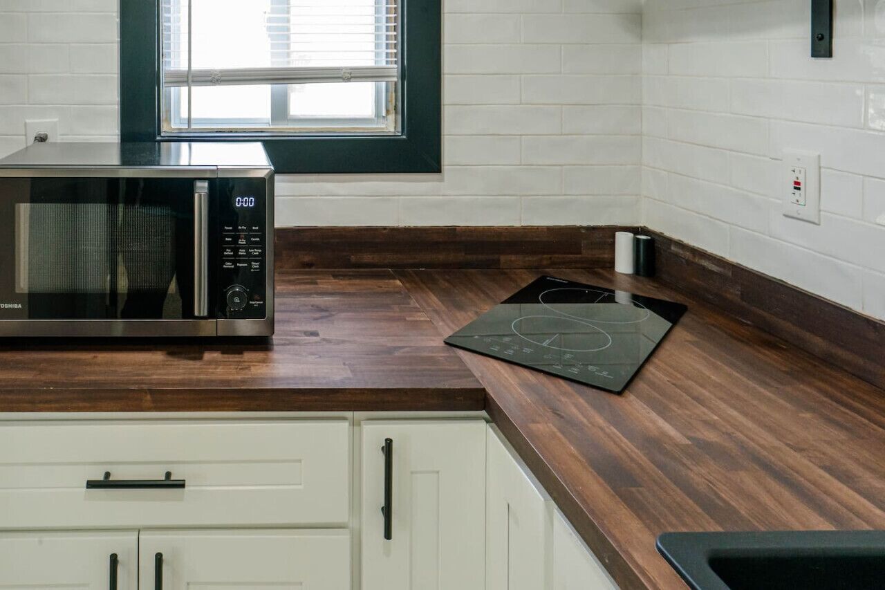 Een keuken met een magnetron, een zwart inductiekookveld, witte kasten en een raam met zonwering.