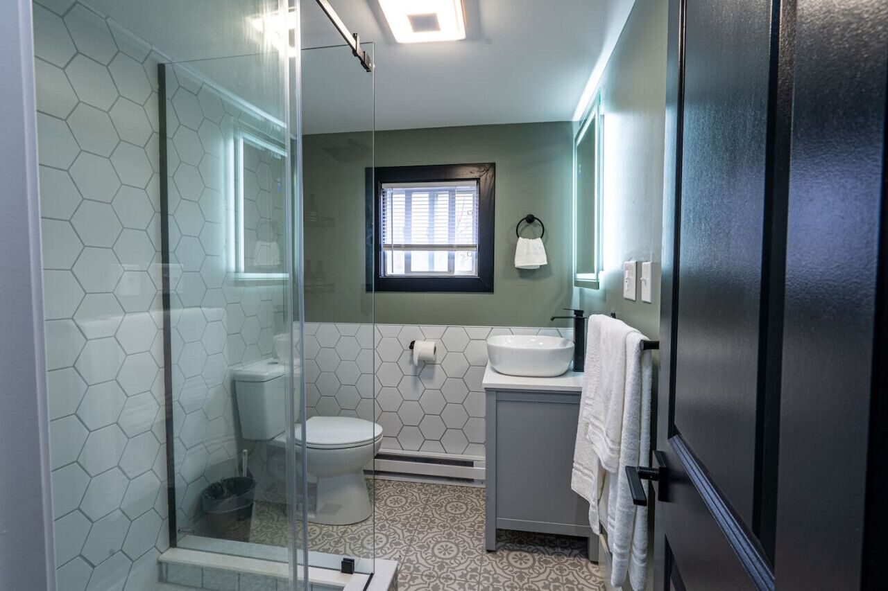 A bathroom with a glass shower enclosure, a toilet, a sink, and a window.