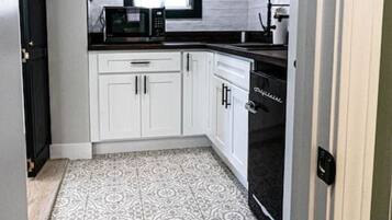 Una cocina estrecha con gabinetes blancos, un microondas negro y un suelo estampado.