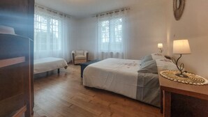 Une chambre d’hôtel avec deux lits, une chaise, une table de chevet avec une lampe et de grandes fenêtres avec des rideaux légers.