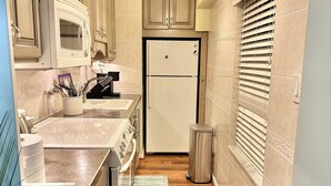 A narrow kitchen with wooden cabinets, a white refrigerator, a microwave, and a stainless steel trash can. There are two mats on the floor. - Breathtaking Ocean view, few steps to the beach!!!!! (Ocean City)