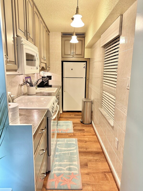A narrow kitchen with wooden cabinets, a white refrigerator, a microwave, and a stainless steel trash can. There are two mats on the floor. - Breathtaking Ocean view, few steps to the beach!!!!! (Ocean City)