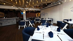 Un restaurante con mesas dispuestas para comer, una zona de bar y una pared de ladrillo al fondo.