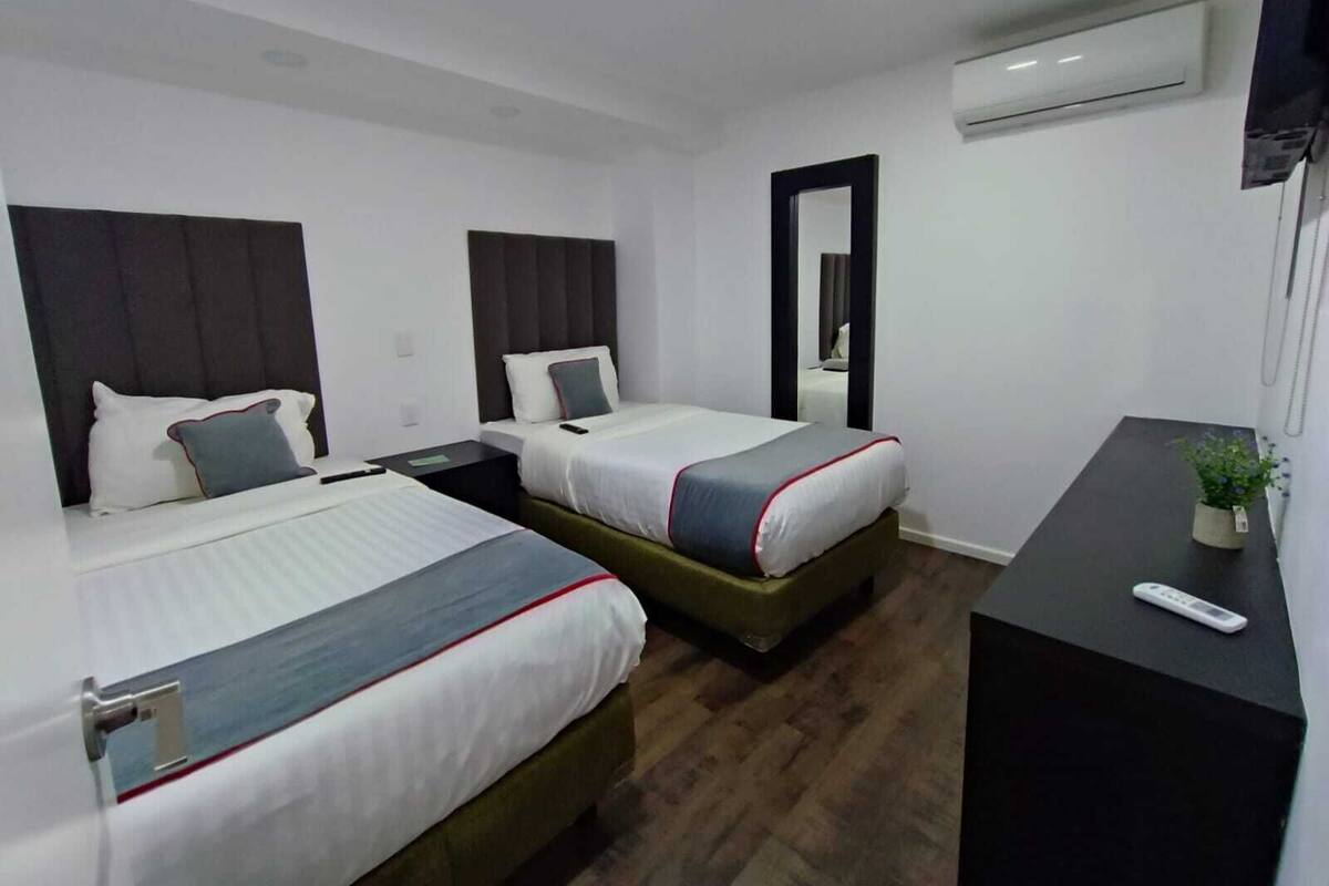 Habitación de hotel con dos camas, un escritorio y un aire acondicionado.