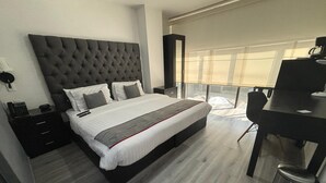 Un dormitorio moderno con una cama grande, mesitas de noche, un escritorio y vistas al exterior.