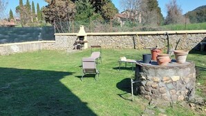 A backyard with a stone barbecue, two lounge chairs, and a small table. - Spacious apartment strategically located for visiting Siena and province (Sovicille)