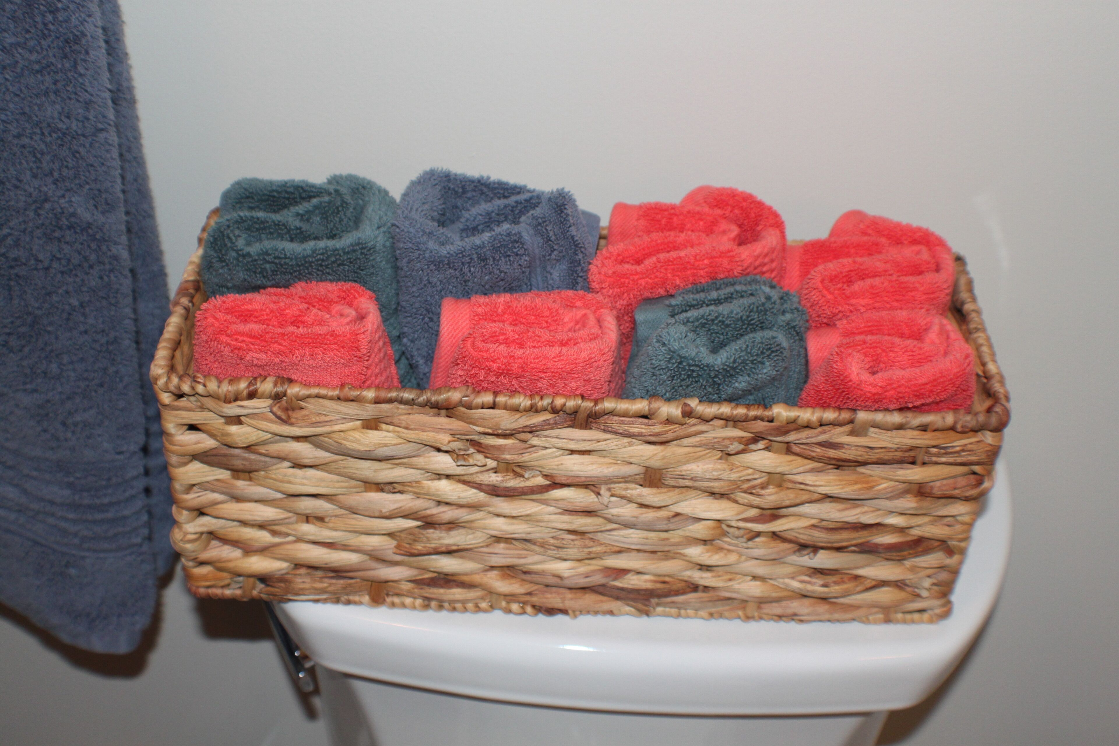 A wicker basket filled with folded towels placed on a toilet.