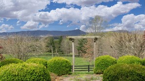 A wooden pergola in a landscaped garden with neatly trimmed bushes and a clear view of distant mountains under a partly cloudy sky. - Duplex in Lexington, VA, Loranwoods (Rockbridge County)