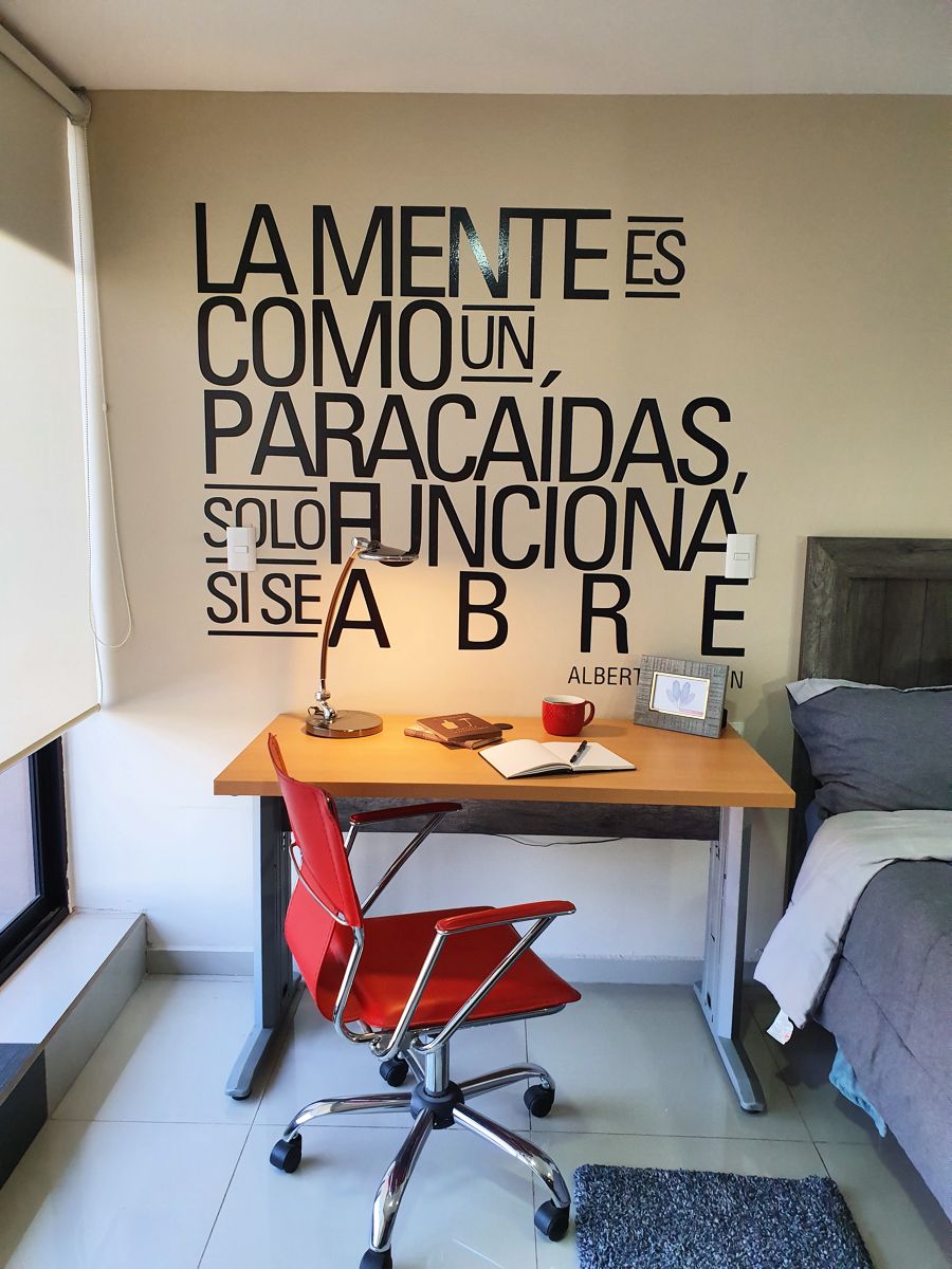 Un dormitorio con cama, escritorio y silla. Hay una cita motivacional en la pared.