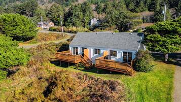 A two-story house with a deck, surrounded by a forested hillside.