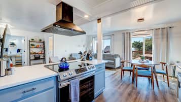 A modern kitchen with a built-in oven, a stainless steel range, and a blue kettle. There is a dining area with a round table and chairs.