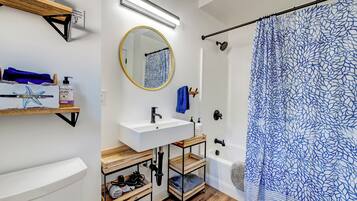 A bathroom with a white sink, wooden shelves, a round mirror, and a shower with a blue patterned curtain.