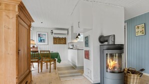 Une cuisine chaleureuse avec un poêle à bois, un coin repas avec une nappe verte et un buffet en bois.