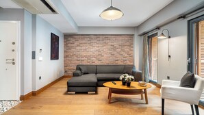 A modern living room with a brick wall, a grey sofa, a round wooden coffee table, and a white armchair. - Urban Quarters - Asmali Mescit (Istanbul)