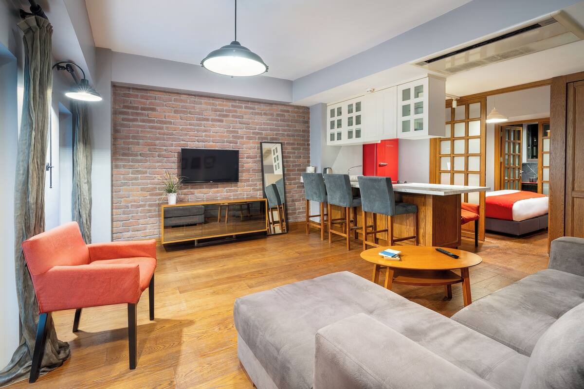 A modern living room with a brick wall, a flat-screen TV, a dining area with a table and chairs, and a sofa.