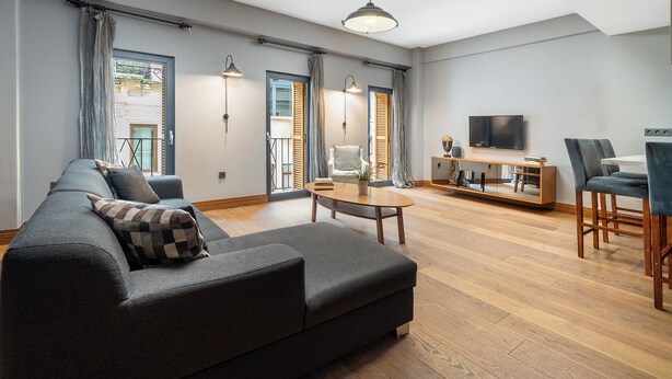 A modern living room with a dark grey sofa, a wooden coffee table, and a TV mounted on the wall. - Urban Quarters - Asmali Mescit (Istanbul)