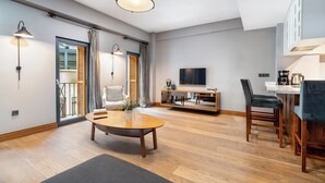 A modern living room with a round wooden coffee table, a white sofa, a TV mounted on the wall, and a dining area with a wooden table and chairs. - Urban Quarters - Asmali Mescit (Istanbul)