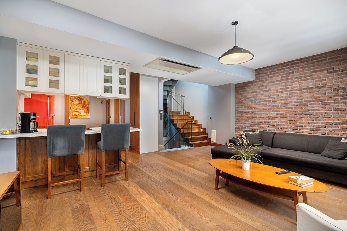 A modern living space with a kitchen, dining area, and a staircase leading to an upper level.
