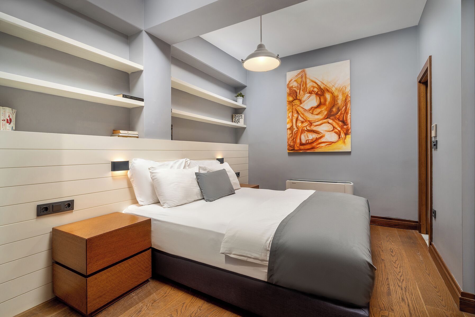 Een moderne slaapkamer met een bed, nachtkastjes, een wandplank en een groot abstract schilderij.