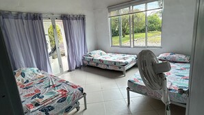 Une chambre avec trois lits, un ventilateur de plafond et une fenêtre donnant sur un paysage verdoyant.