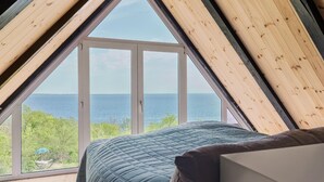 Un dormitorio con un tragaluz grande, una cama con colcha azul y vistas al mar.