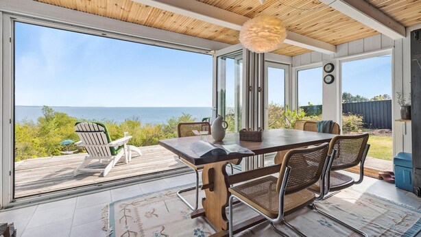 Un comedor con vista al mar, que incluye una mesa de madera, sillas y una lámpara colgante.