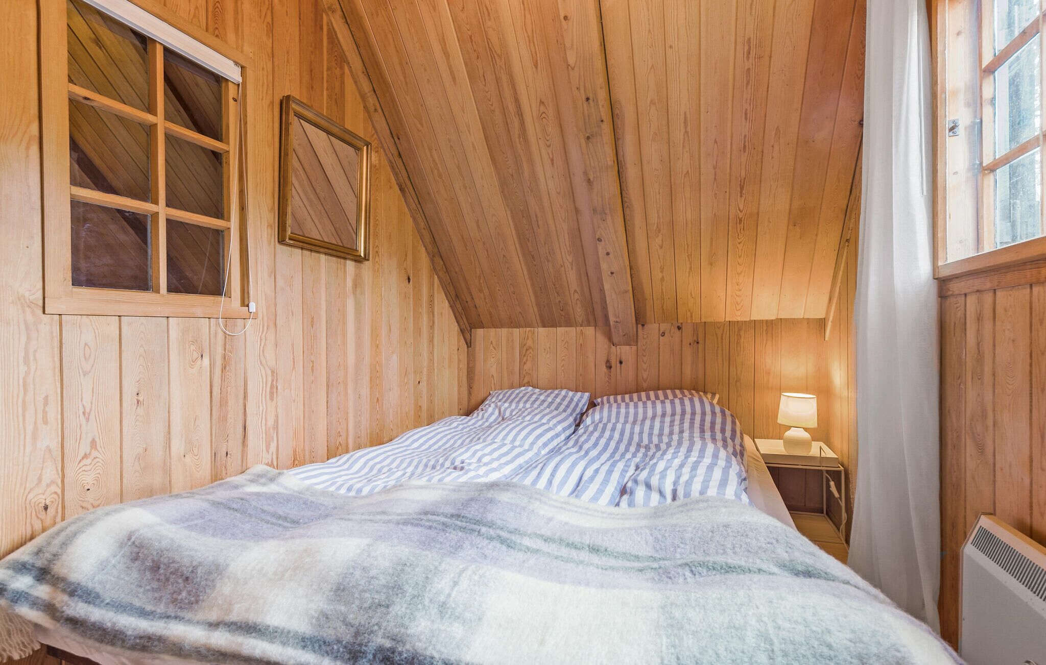 A cozy wooden room with a bed, a window, and a wall-mounted picture frame.