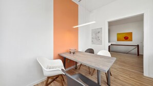 Ein moderner Essbereich mit einem Holztisch, weißen Stühlen und einer leuchtend orangefarbenen Wand.