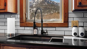Une cuisine avec un robinet noir, une fenêtre donnant sur les montagnes et deux bocaux étiquetés « Thé » et « Sucre ».