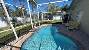 A swimming pool with a brick border, surrounded by a white fence, and a patio area with lounge chairs. - Amazing pool house 10 minutes from disney (Kissimmee)