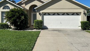 A two-story house with a garage, a front door, and a small garden with a palm tree. - Amazing pool house 10 minutes from disney (Kissimmee)