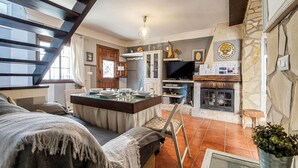 Een gezellige woonkamer met een open haard, een eethoek met een glazen tafel, en een keuken met een televisie.