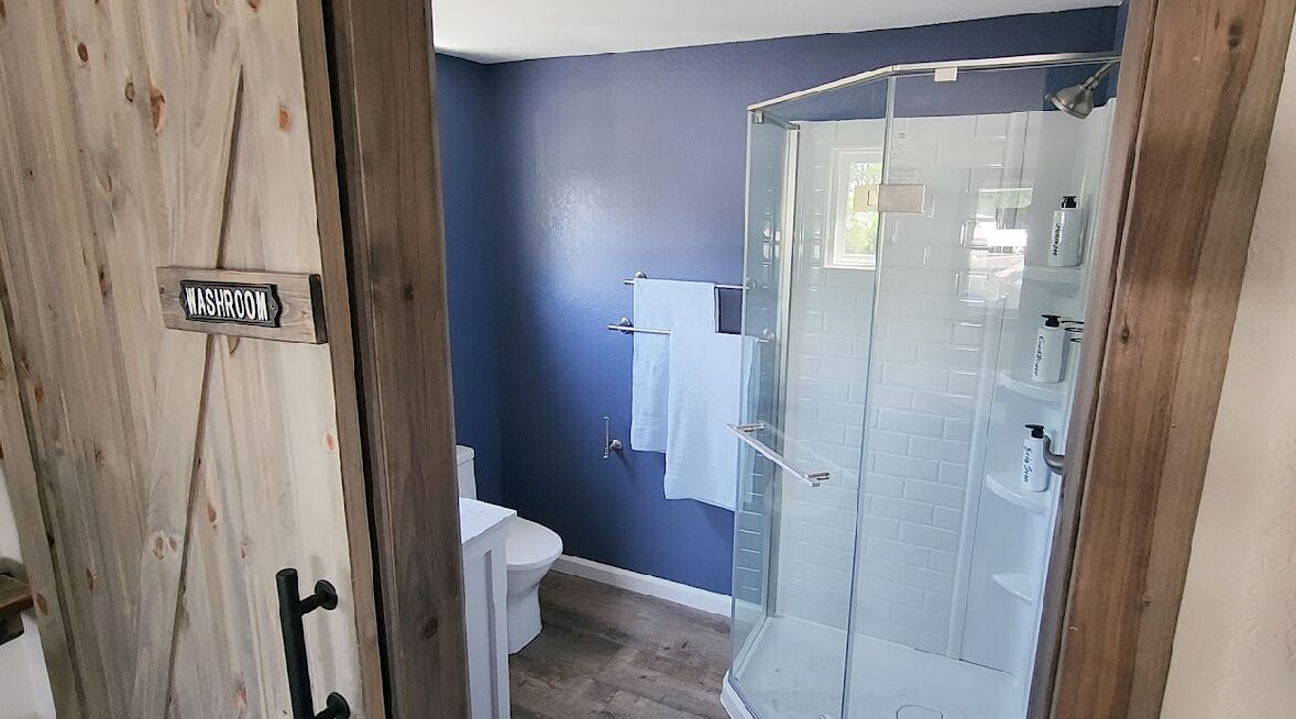 Ein Badezimmer mit blauer Wand, einer Duschkabine aus Glas, einer Toilette und einem Waschbecken.