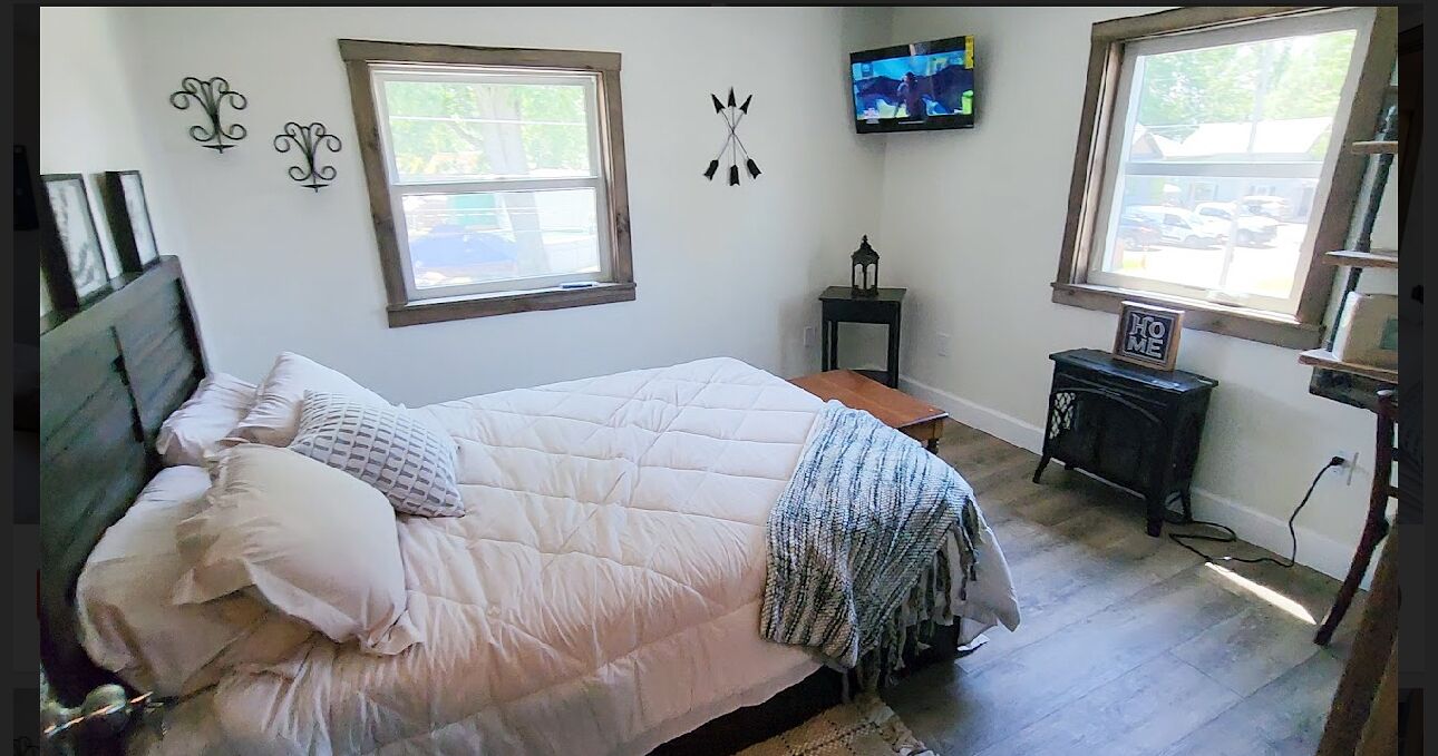 A bedroom with a bed, a TV, a window, and a small table.
