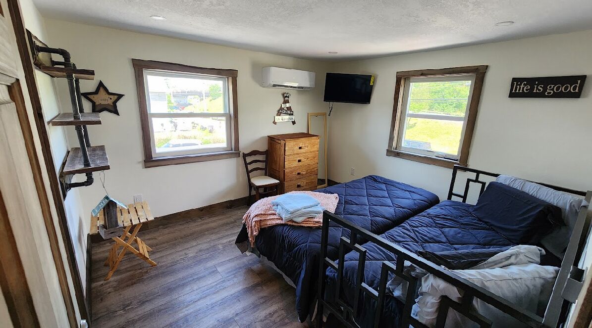 Een slaapkamer met een bed, dressoir, stoel en een aan de muur bevestigde televisie.