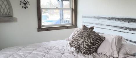 A bedroom with a bed, a window, a wall-mounted air conditioner, and a decorative sign.