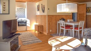 Een gezellige woonkamer met een televisie, een eettafel met stoelen, een keuken met een fornuis, en houten wanden.
