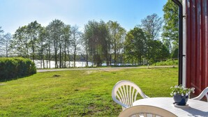 Een terras met tafel en stoelen, met uitzicht op een gazon met bomen en een waterpartij.