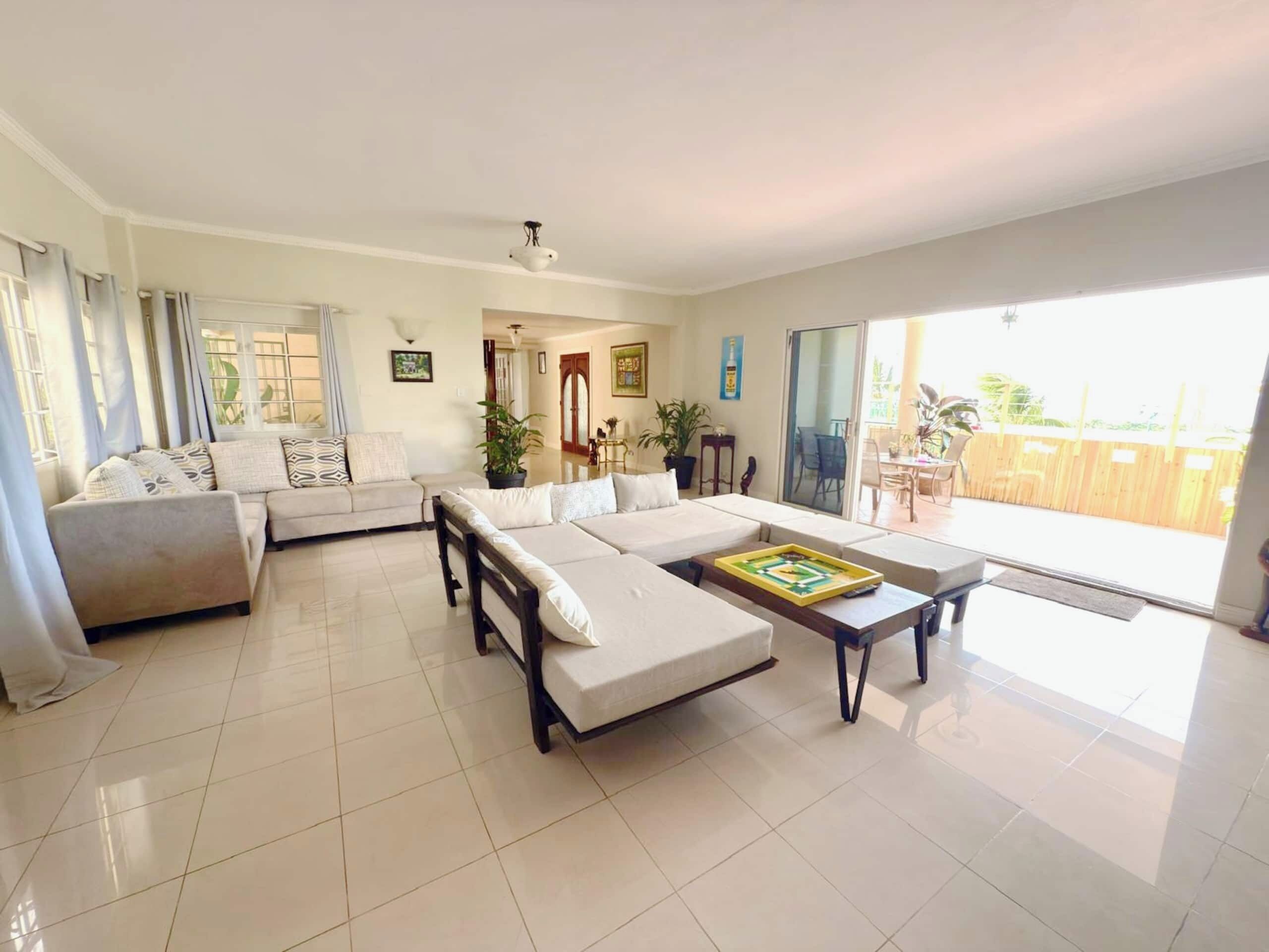 A spacious living room with a sofa set, a coffee table, and a sliding glass door leading to an outdoor area.