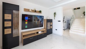 A modern living room with a large flat-screen TV, built-in shelves, and a staircase leading to another level. - Amazing home in Primosten with sauna (Primosten)