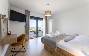A modern hotel room with a bed, a desk, a chair, a TV, and a balcony with a view. - Amazing home in Primosten with sauna (Primosten)