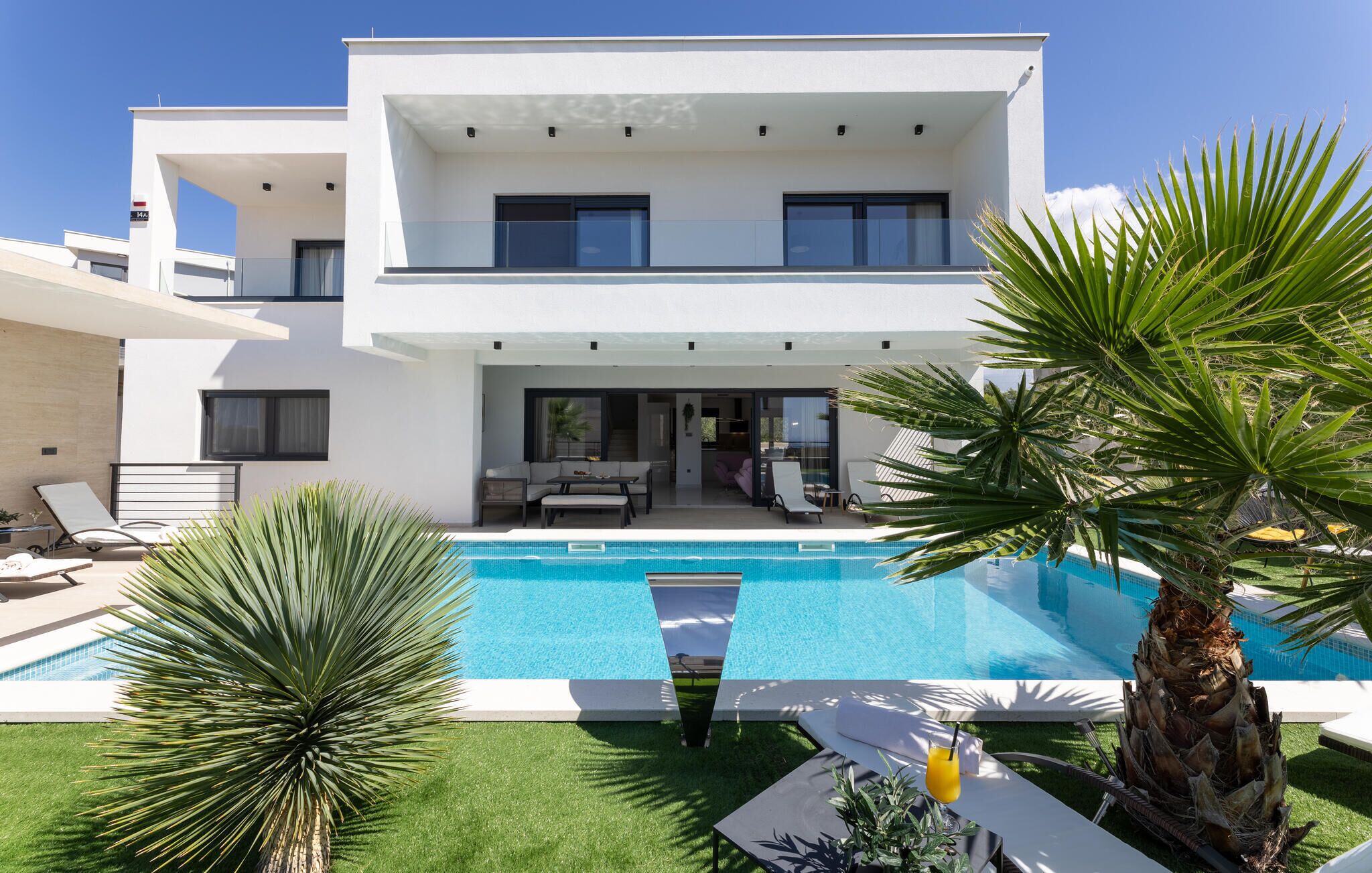 Een modern herenhuis met een zwembad, terras en tropische beplanting.