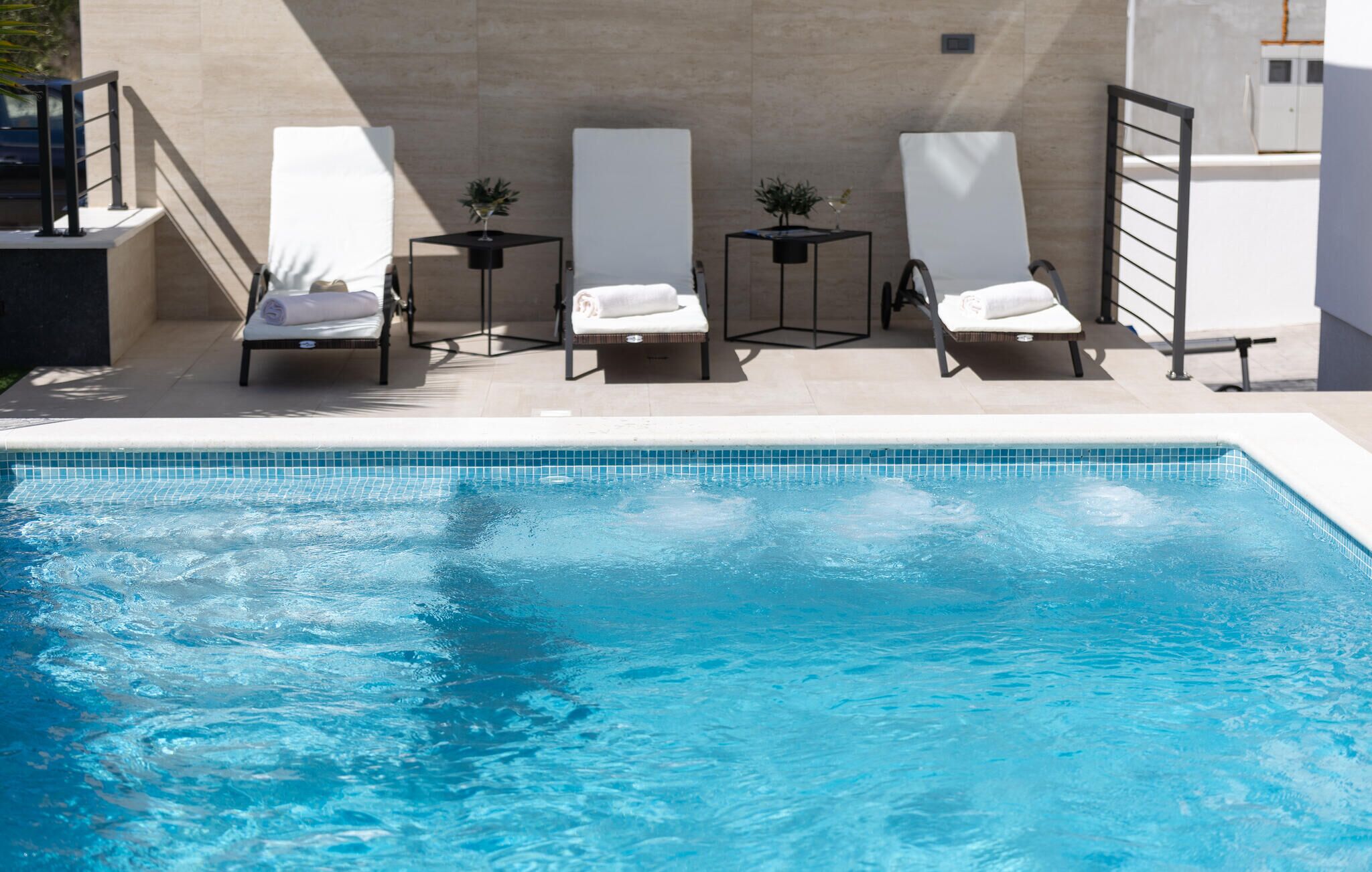 A swimming pool with four sun loungers and a small table with a plant.