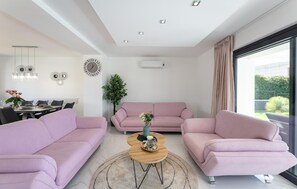 A modern living room with a pink sofa set, a wooden coffee table, and a dining area with a white table and chairs. - Amazing home in Primosten with sauna (Primosten)