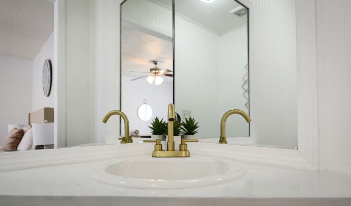 A bathroom with a white sink, gold faucets, and a large mirror.